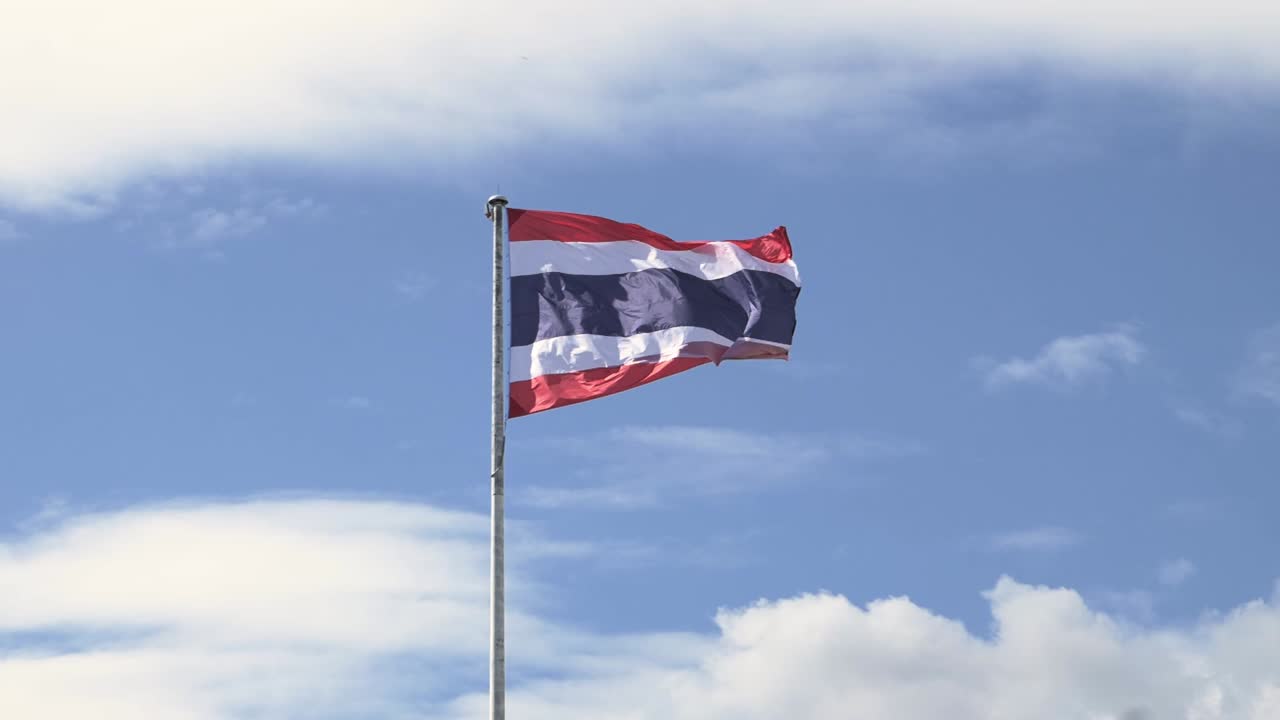 ondeando la bandera del reino de tailandia en un poste con cielo azul y nubes blancas en el fondo
