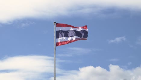 Waving-the-Kingdom-of-Thailand-flag-on-a-pole-with-blue-sky-and-white-clouds-in-the-background