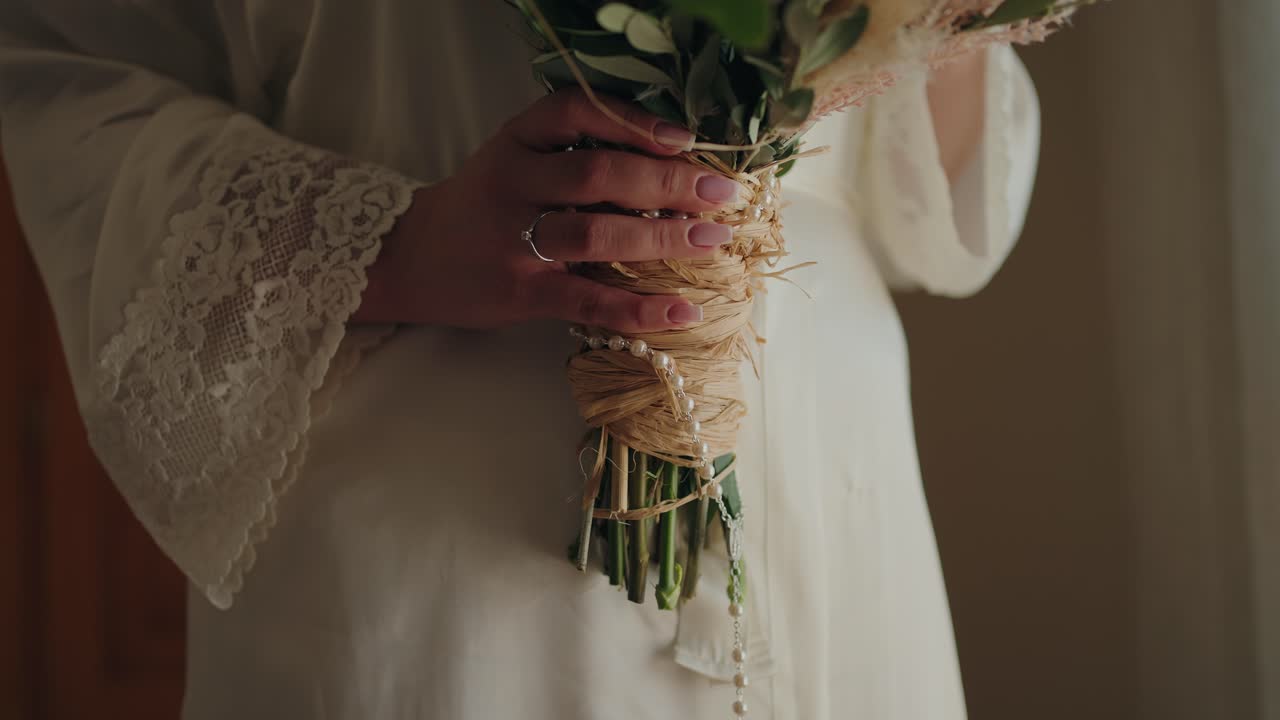 Close up of bride holding bouquet with lace sleeve and delicate pearl details