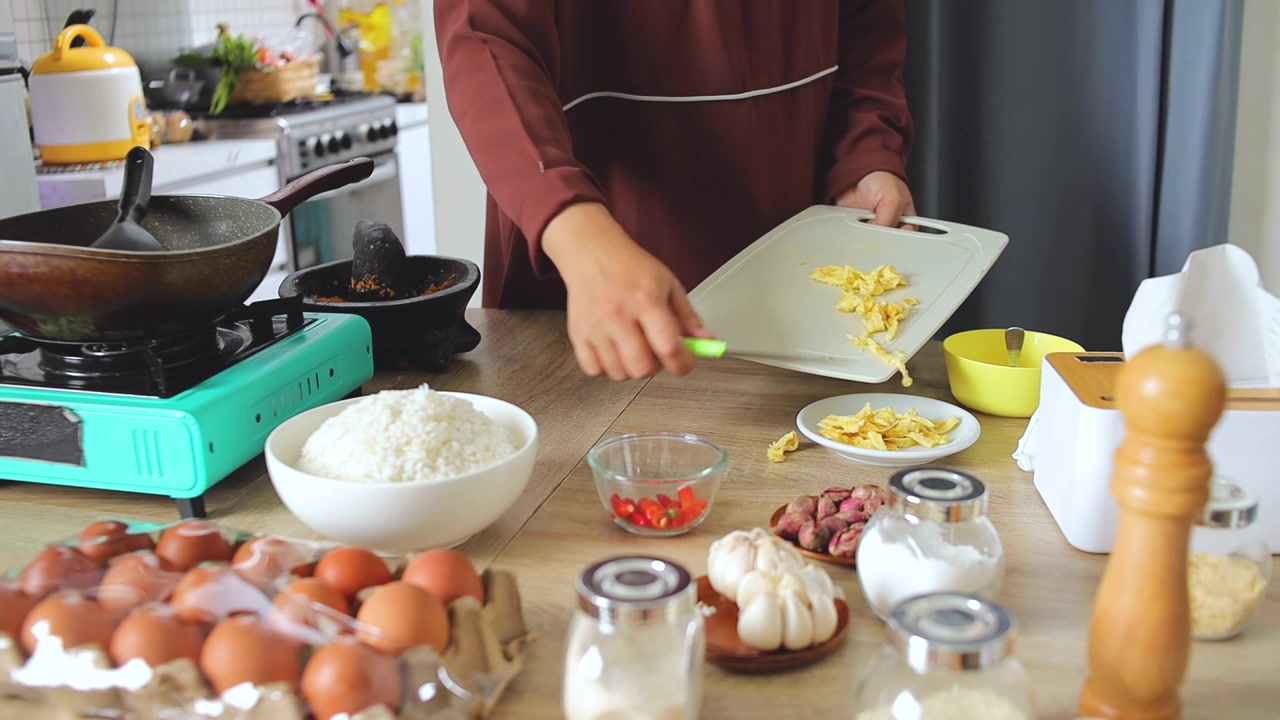 Tangan memindahkan potongan telur dadar ke piring di dapur untuk topping nasi goreng