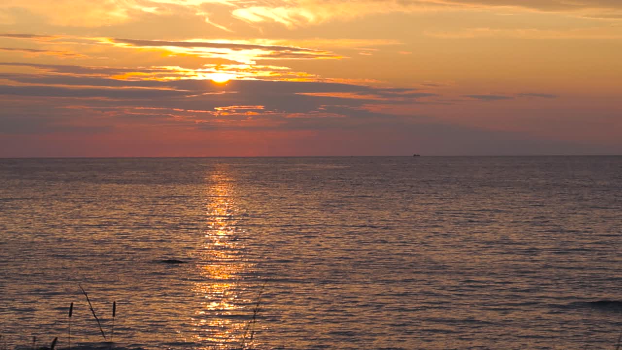 서루피 해변에서 해가 지고 바다가 어두워지면서 오렌지색, 노란색, 빨간색으로 하늘을 가리키고 수평선에 선박이 보이고 물이 느린 속도로 움직이고 하늘에는 4k의 구름이 있습니다.