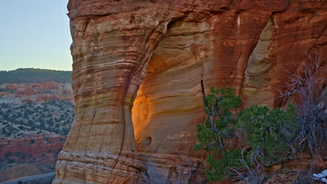 the camera smoothly approaches a natural red rock arch, with the morning sun casting a warm glow through its opening.