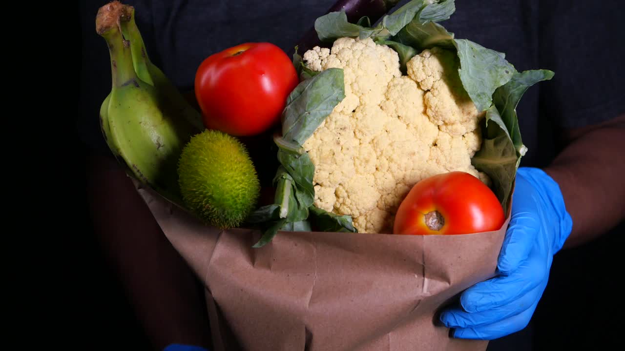 persona que sostiene una bolsa de comestibles con verduras y frutas