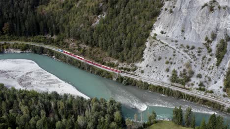 red train drives in the scenic rhine canyon in switzerland, aerial view