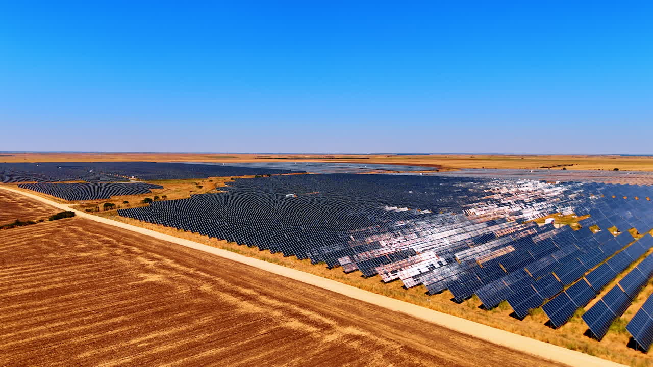 Vasto parco solare sotto un cielo terso. Grandi pannelli solari si estendono su un vasto paesaggio sotto un cielo blu brillante, a dimostrazione della produzione di energia rinnovabile