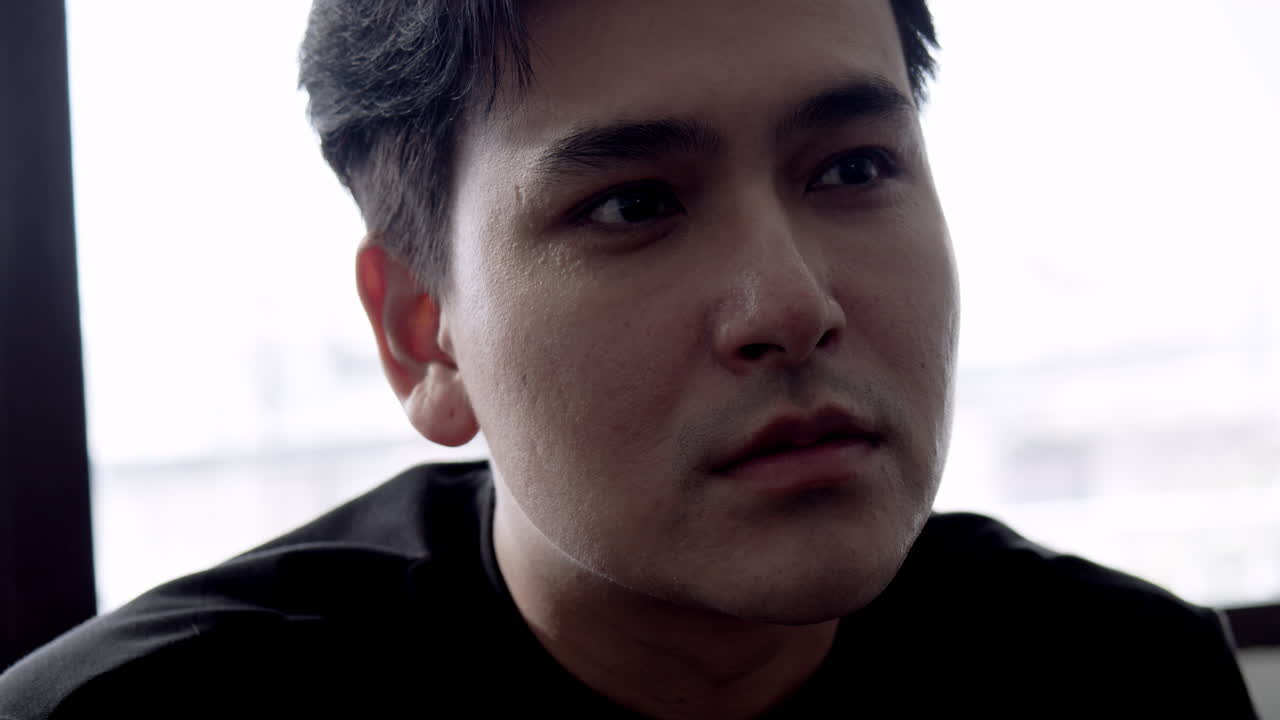 A young man's contemplative expression captures a moment of reflection in an urban office.