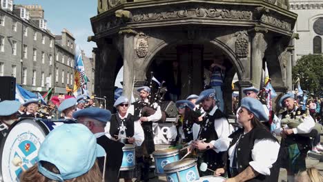 a crowd watch a scottish pipe band plays music at the aberdeen mercat.