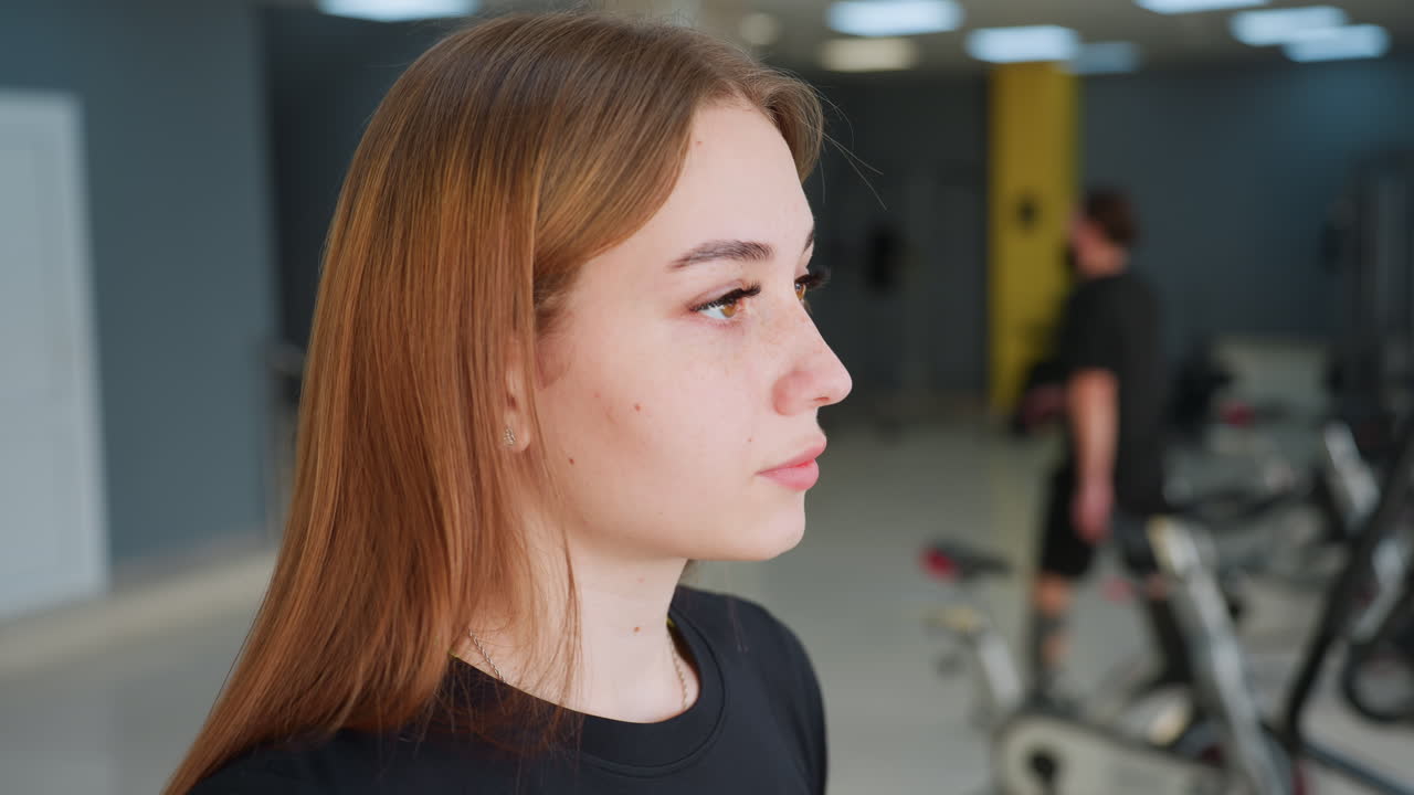 close up of student staying focused during workout session in gym with blurred view of people using exercise machines and one person walking out of gym space in background