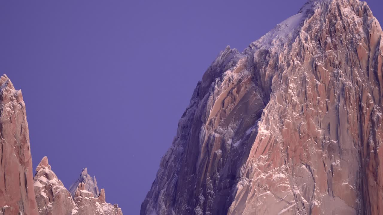 Backward zoom-out static view reveals Mount Fitz Roy under the morning purple sky with its rocky steep peaks in Patagonia, Argentina