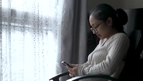 woman in sweater using smartphone by window, natural light, serene mood