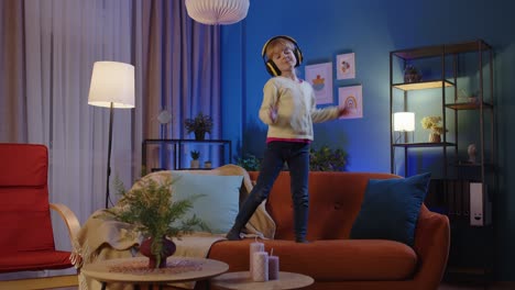 una niña feliz con auriculares bailando un baile de moda mientras escucha música en casa sola
