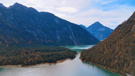 Stunning view of the Alps with a beautiful lake. Pine tree woods grow around Lake Plansee, Tyrol, Austria. Aerial perspective.