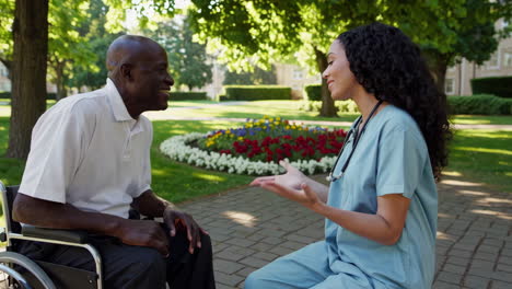 healthcare professional conversing with elderly man in wheelchair in a park