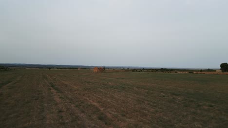 Aerial-low-flying-over-field-in-Tarrega,-Spain,-passing-by-traditional-tool-shed