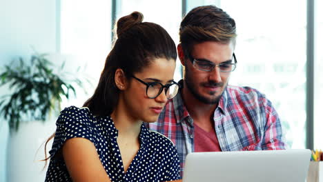 Male-and-female-executives-discussing-over-laptop-at-desk