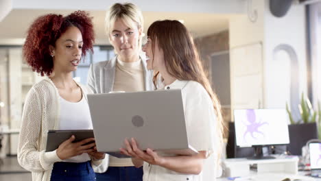 collaborating in office, three women discussing project holding laptops and tablet