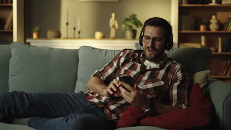 man relaxing on couch with headphones and cell phone