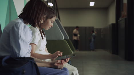 Smiling-schoolgirls-using-tablet-at-school-break.-Two-teens-talking-at-lockers.