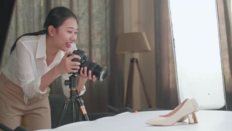 asian female photographer adjusting position of women's shoes and taking photos of them in home studio