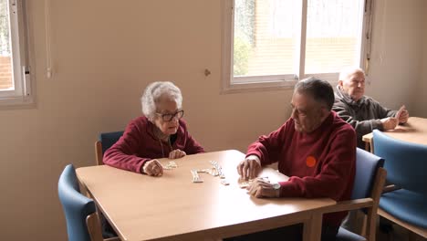 senior friends playing dominoes at table in nursing home