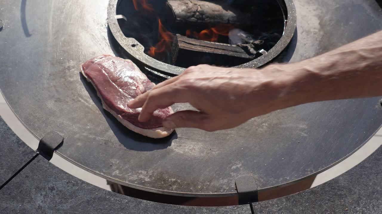 Slow motion shot of a chef placing raw steaks onto the bbq to start cooking