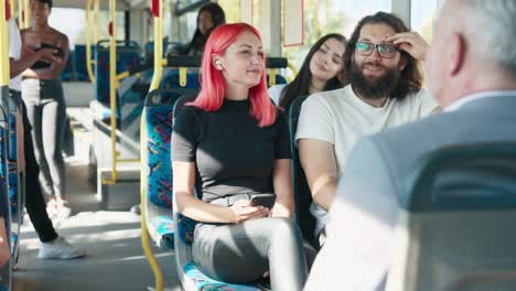 girl with pink hair rides public transport bus, talks to friend sitting next to her