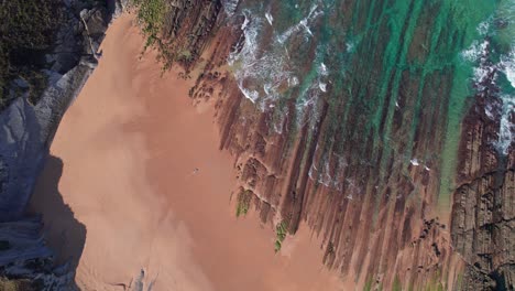 Beach-shore-aerial,-push-out-topview,-oceanic-sea-waves-washing-on-a-rocky-sand-coast-in-slow-motion-slomo,-Playa-de-Tagle,-Spanish-coast