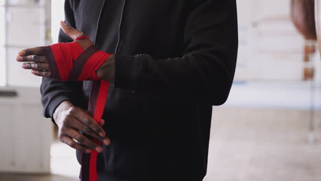 Close-Up-Of-Male-Boxer-Training-In-Gym-Putting-Wraps-On-Hands-Standing-Next-To-Punching-Bag