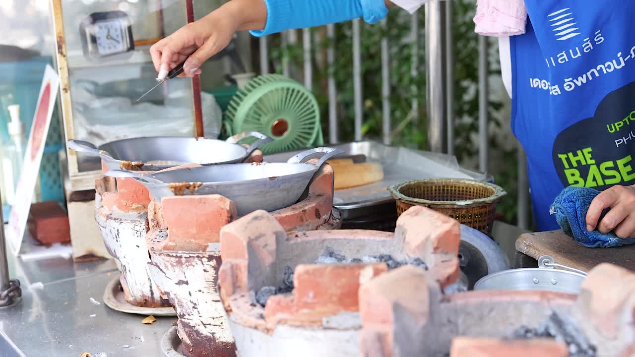A vendor prepares traditional Thai snacks using a hot pan in a bustling Phuket market. Bright daylight enhances the vibrant scene