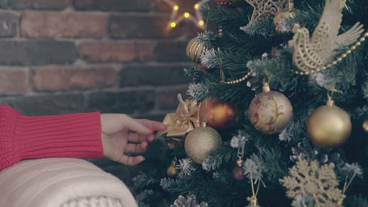 una joven toca una bola dorada y un arco en el árbol de navidad.