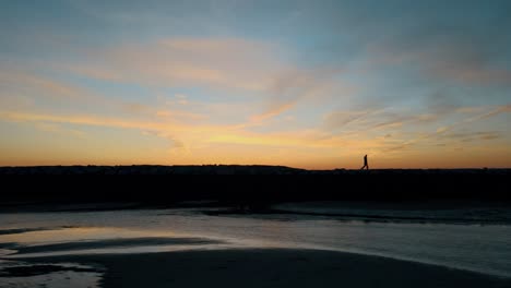 vista aérea que muestra la silueta de una pareja caminando por la presa en provincetown durante la puesta de sol dorada - rompeolas del océano atlántico en américa - vuelo lateral