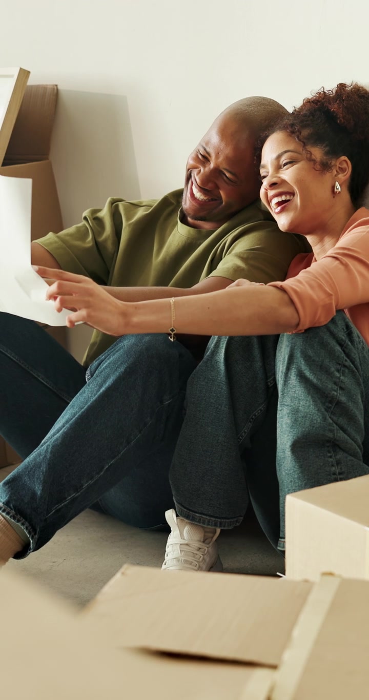 Happy Couple Sitting on Floor Looking at Paper in New Home