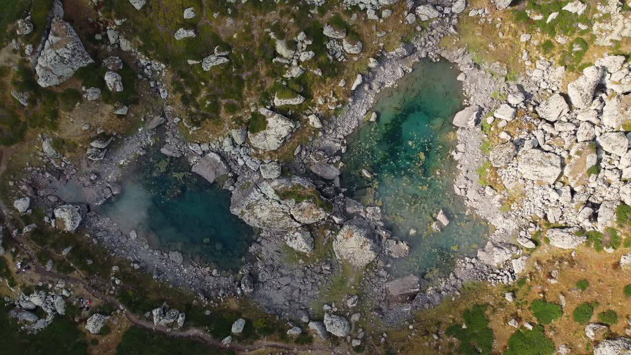 Beautiful top-down panoramic drone fly at crystal mountain ponds with turquoise water surrounded by rocks, Khevsureti, Mtskheta-Mtianeti, Georgia