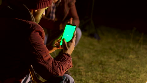 Tourist-scorlling-down-on-phone-with-green-screen-around-camp-fire