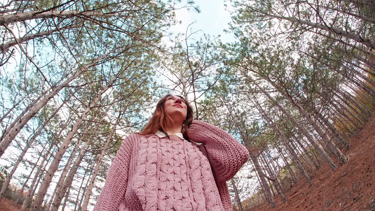 천천히 움직이는 젊은 여성은 하늘을 향해 가을에 소나무 사이에서 숲 속의 개에서 아래에서 위로 움직입니다.