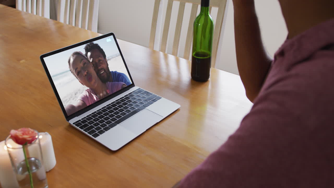 Biracial man sitting at table using laptop making video call with friends
