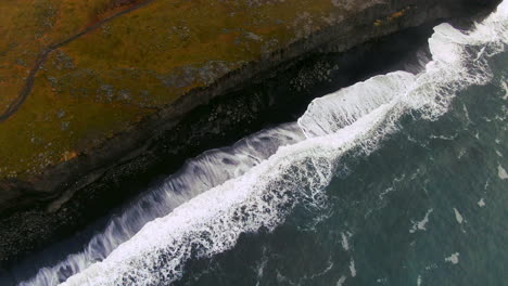 Aerial-cinematic-drone-pan-down-waves-crashing-on-shore-fog-early-winter-at-Black-Sand-Beach-Apostles-fire-and-ice-ocean-next-to-Dyhrolaey-lighthouse-and-cave-Reynisfjara-Iceland