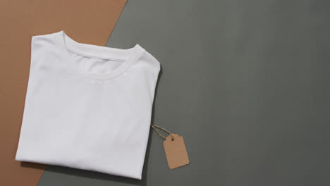Video-of-flat-lay-of-folded-white-t-shirt-with-tag-and-copy-space-on-grey-and-brown-background