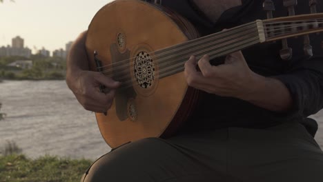 close up shot of man playing oud fiddle guitar outdoors in front of river