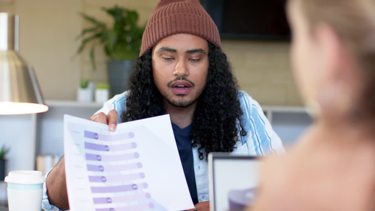Diverse coworkers lifting printed horizontal bar chart at desk indicating data bars for discussion