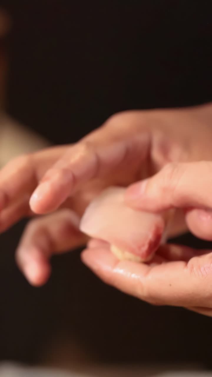 Close-up of a chef's hands expertly pressing and shaping nigiri sushi against a dark background