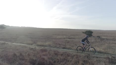 Following-drone-shot-of-mountainbiker-riding-past-in-nature