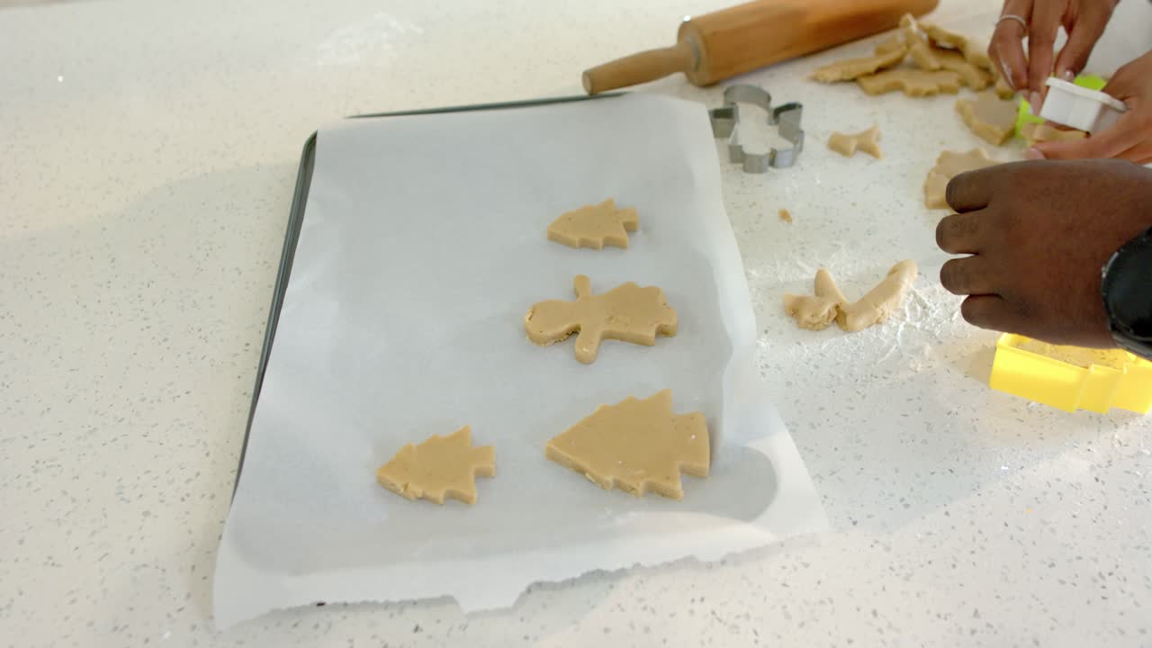 Voyant les chutes, un couple mixte découpe et arrange des formes de biscuits sur un plateau sur le comptoir, avec espace de copie.