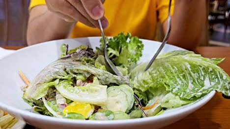 hand woman mixing green salad in a glass bowl