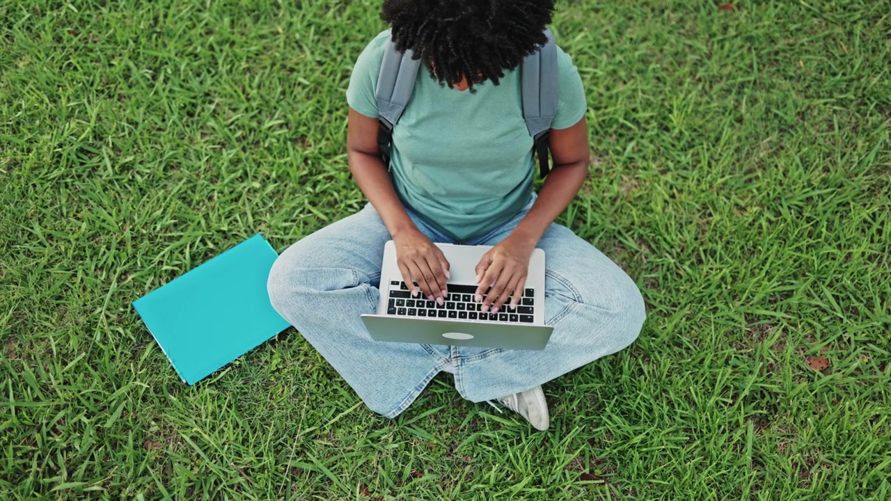 Young Woman Typing on Laptop While Sitting on Green Grass