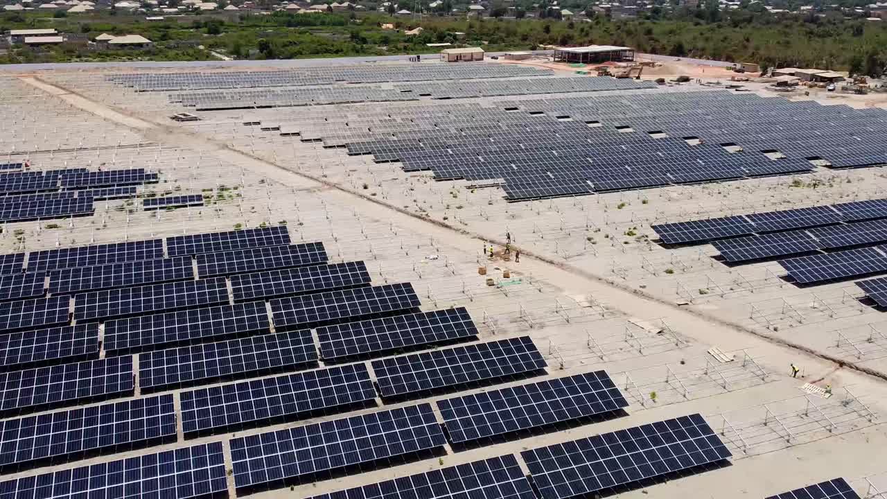 vuelo aéreo sobre una granja solar con paneles solares bifaciales limpios, sucios y polvorientos en el sitio del proyecto fotovoltaico solar de jambur, gambia, en construcción