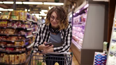 compras, tecnologia, vendas, consumismo e conceito de pessoas - mulher com smartphone e fones de ouvido no pescoço andando no supermercado