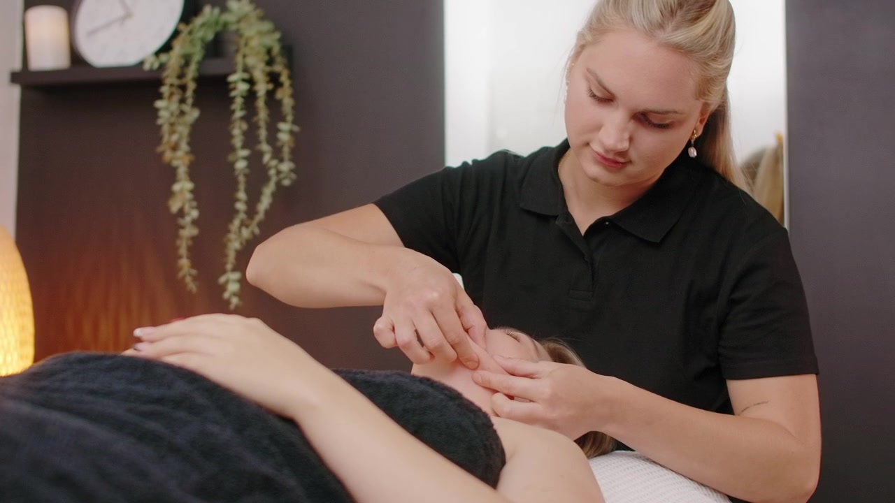 Professionel kosmetolog udfører ansigtsmassage på klient i spa