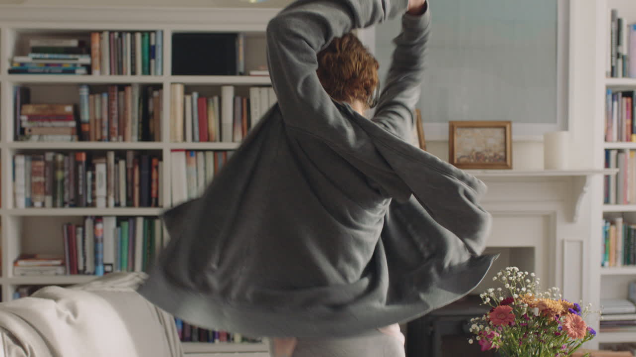 행복한 젊은 여성이 집에서 춤을 추고 재미있게  ⁇ 키  ⁇ 합 댄스 동작을 즐기고 스마트폰을 사용하여 거실에서 연습하고 있습니다.