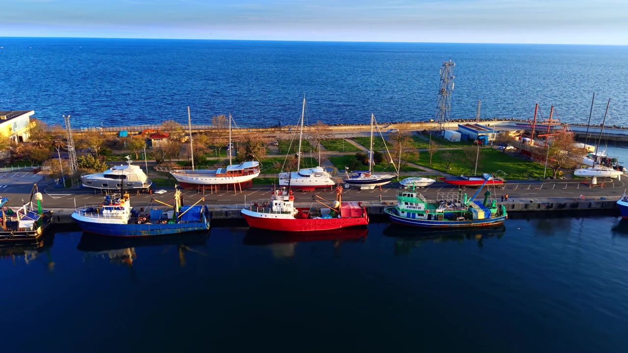 Cantiere navale con yacht ormeggiato, Bulgaria. Barca da pesca colorata e barca a vela allineate lungo il molo accanto al mare blu.